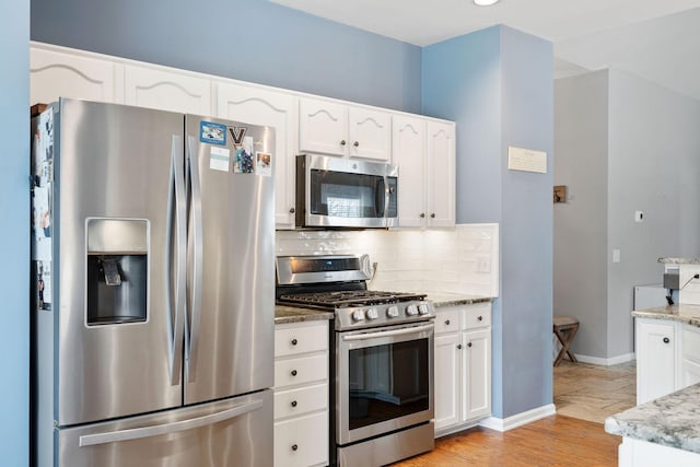 kitchen with light stone counters, baseboards, white cabinets, appliances with stainless steel finishes, and backsplash