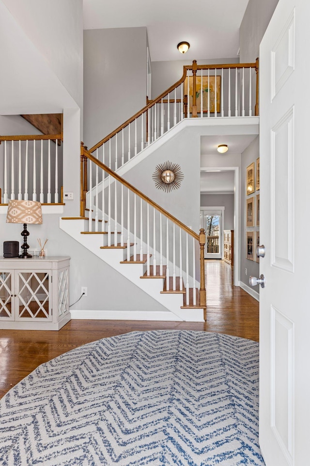 foyer entrance with a towering ceiling, stairs, baseboards, and wood finished floors