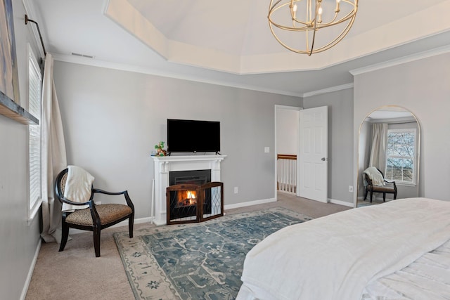 carpeted bedroom featuring crown molding, a notable chandelier, a raised ceiling, a lit fireplace, and baseboards