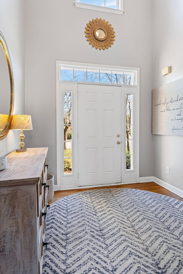 entryway featuring a towering ceiling, plenty of natural light, baseboards, and wood finished floors