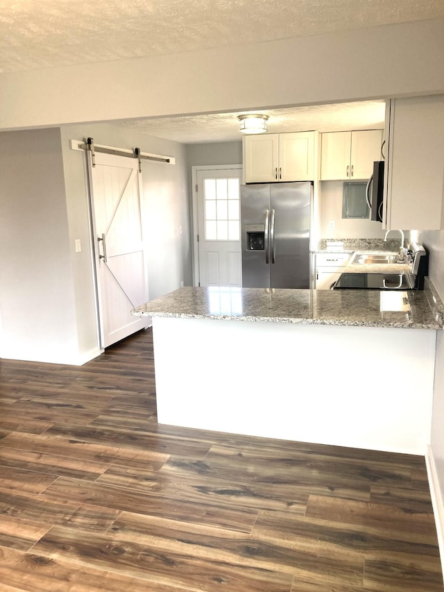 kitchen featuring light stone countertops, dark wood finished floors, a peninsula, stainless steel appliances, and a barn door