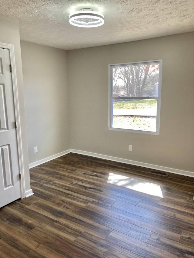 unfurnished room with visible vents, baseboards, a textured ceiling, and dark wood finished floors