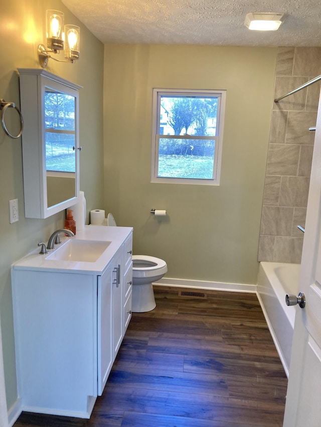 full bath with toilet, a healthy amount of sunlight, wood finished floors, and a textured ceiling