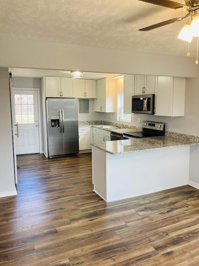 kitchen featuring light stone counters, appliances with stainless steel finishes, a peninsula, dark wood-style floors, and white cabinetry