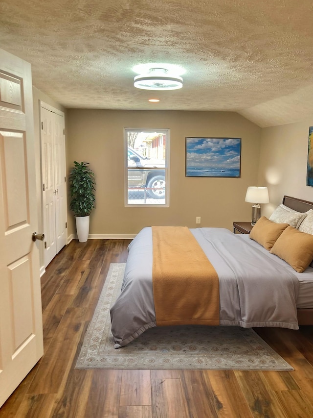 bedroom with vaulted ceiling, wood finished floors, baseboards, and a textured ceiling