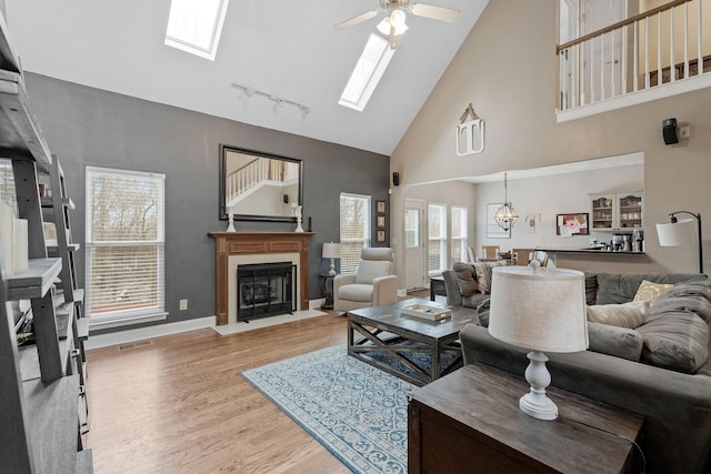 living area featuring wood finished floors, a skylight, a fireplace with flush hearth, and visible vents