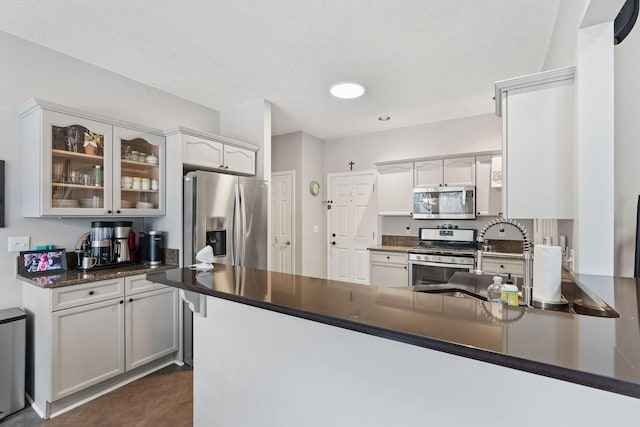 kitchen with dark countertops, stainless steel appliances, a peninsula, and glass insert cabinets