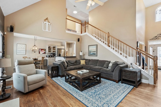 living area with baseboards, a towering ceiling, ceiling fan, stairway, and wood finished floors