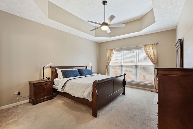 bedroom featuring a raised ceiling, light carpet, a textured ceiling, and baseboards