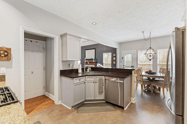 kitchen with pendant lighting, an inviting chandelier, appliances with stainless steel finishes, a sink, and a peninsula