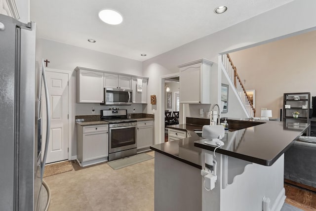 kitchen with a breakfast bar, stainless steel appliances, dark countertops, a sink, and a peninsula