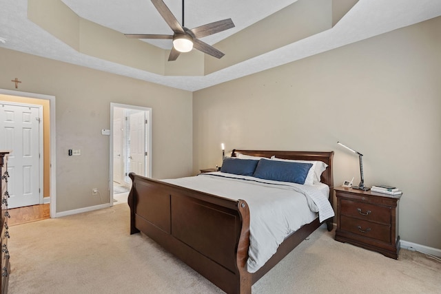 bedroom featuring light carpet, baseboards, a tray ceiling, and ensuite bathroom