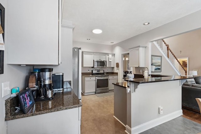 kitchen featuring a kitchen breakfast bar, a peninsula, stainless steel appliances, white cabinetry, and a sink