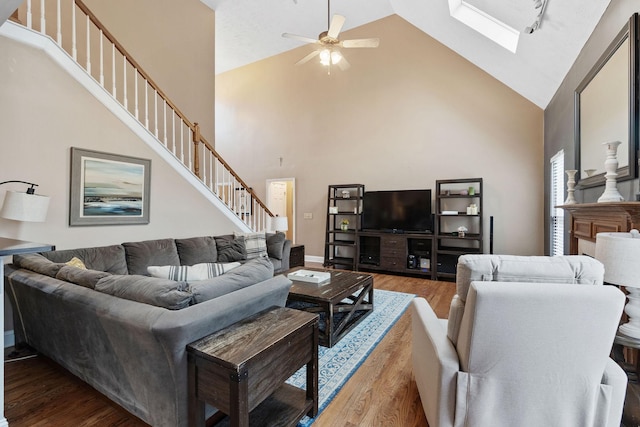 living room with a skylight, ceiling fan, wood finished floors, high vaulted ceiling, and stairs