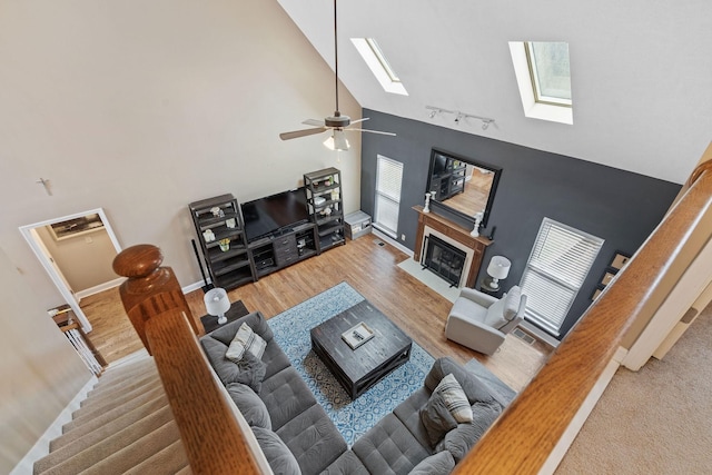 living area with a skylight, rail lighting, a fireplace with flush hearth, wood finished floors, and high vaulted ceiling