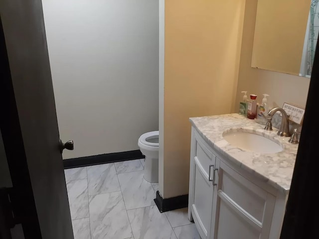 bathroom featuring toilet, marble finish floor, vanity, and baseboards