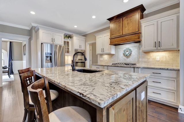 kitchen featuring stainless steel appliances, ornamental molding, a sink, and a kitchen island with sink