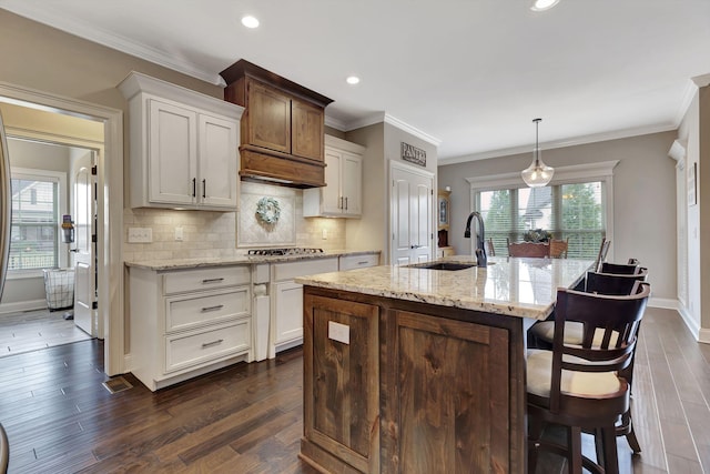 kitchen with a center island with sink, decorative backsplash, dark wood-style floors, crown molding, and a sink