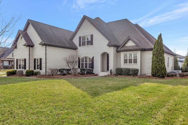 french country inspired facade featuring a front yard, brick siding, and roof with shingles