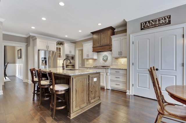 kitchen with a kitchen island with sink, a sink, appliances with stainless steel finishes, backsplash, and dark wood finished floors