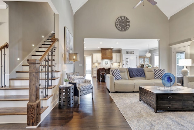 living room with dark wood finished floors, ceiling fan, stairway, crown molding, and high vaulted ceiling