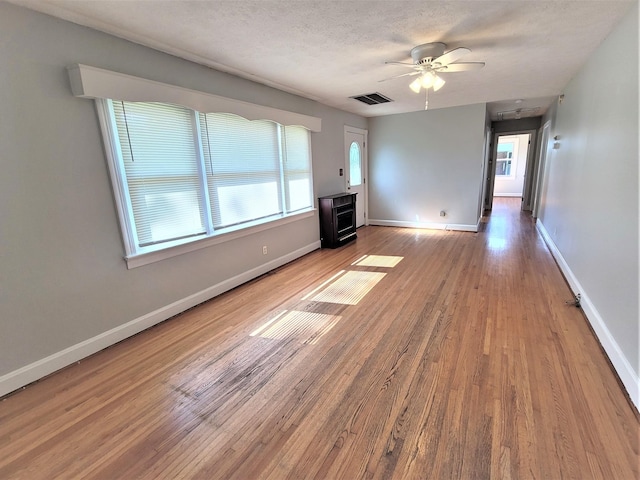 unfurnished living room featuring visible vents, ceiling fan, a textured ceiling, wood finished floors, and baseboards