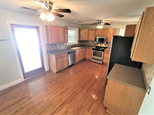 kitchen featuring stainless steel appliances, tasteful backsplash, light wood-type flooring, and a sink