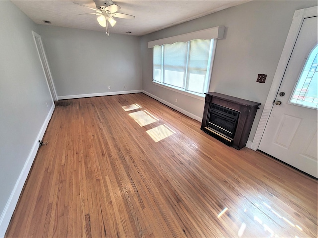 unfurnished living room with ceiling fan, light wood finished floors, a glass covered fireplace, and baseboards