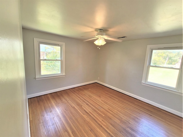 unfurnished room featuring a wealth of natural light, wood-type flooring, visible vents, and baseboards