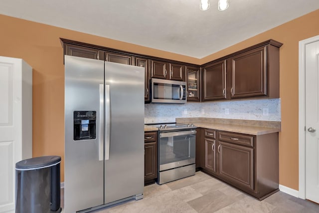 kitchen featuring stainless steel appliances, light countertops, backsplash, glass insert cabinets, and dark brown cabinets