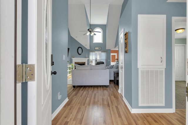 hallway with light wood-style floors, visible vents, high vaulted ceiling, and baseboards