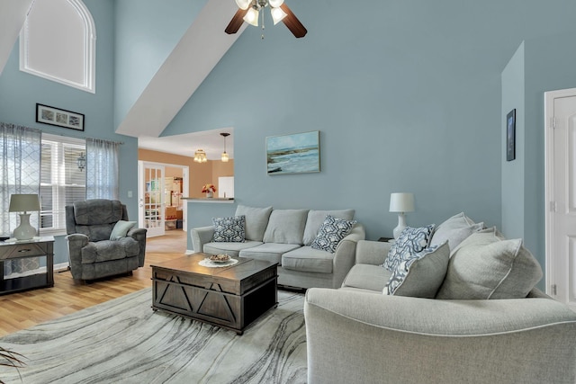 living area with a ceiling fan, a towering ceiling, and wood finished floors