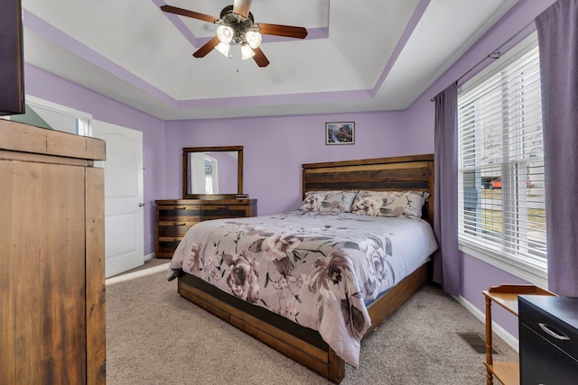 bedroom with ceiling fan, carpet flooring, visible vents, baseboards, and a tray ceiling