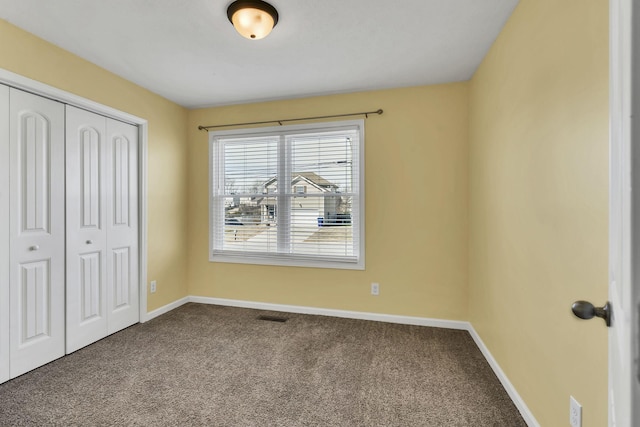 unfurnished bedroom featuring dark colored carpet, a closet, visible vents, and baseboards