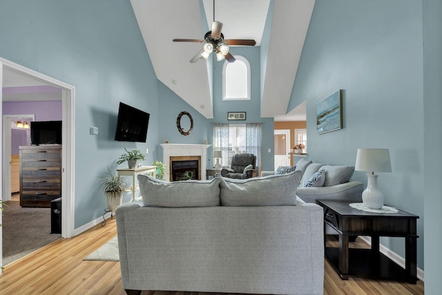 living area with baseboards, ceiling fan, light wood-style flooring, and a tiled fireplace