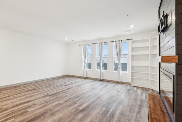 unfurnished living room with visible vents, baseboards, a glass covered fireplace, wood finished floors, and recessed lighting