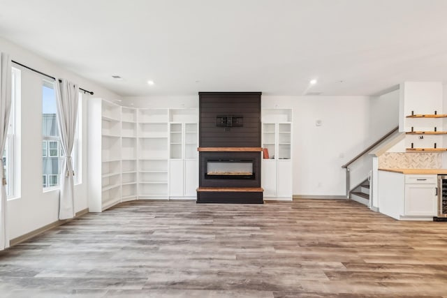 unfurnished living room with wine cooler, stairway, light wood-style floors, a fireplace, and recessed lighting