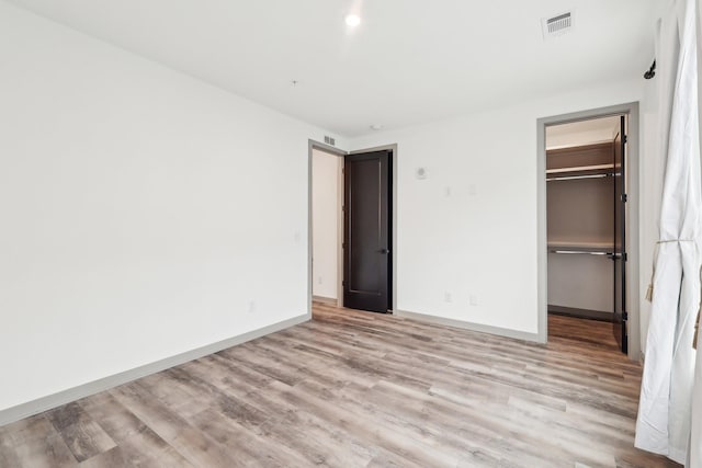 unfurnished bedroom with a walk in closet, light wood finished floors, a closet, visible vents, and baseboards