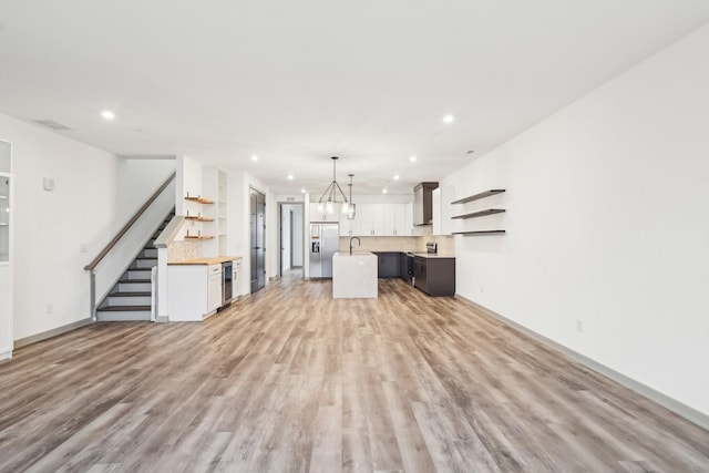 unfurnished living room featuring light wood-type flooring, a sink, stairway, and recessed lighting