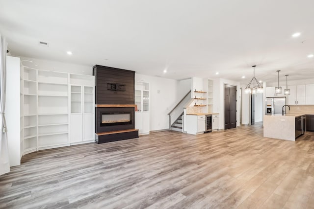 unfurnished living room with wine cooler, a fireplace, a dry bar, recessed lighting, and light wood-style floors