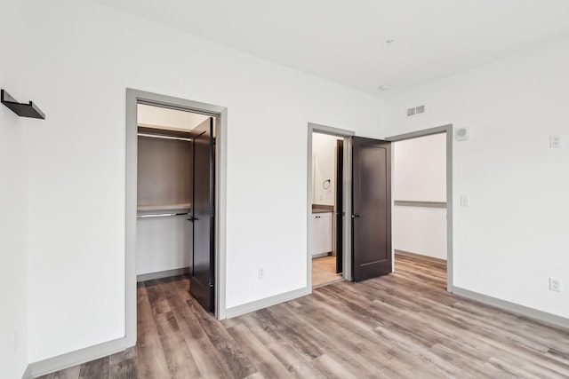 unfurnished bedroom featuring baseboards, visible vents, wood finished floors, a spacious closet, and a closet