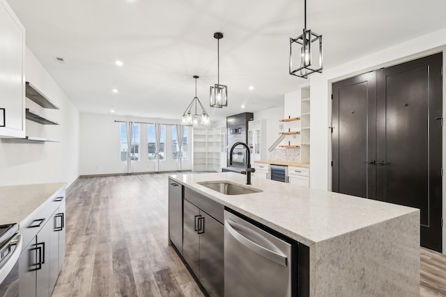 kitchen with light wood-style flooring, a sink, stainless steel dishwasher, open shelves, and an island with sink