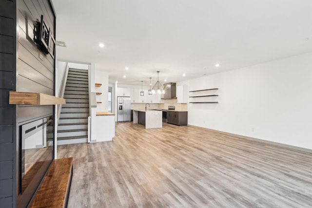 unfurnished living room featuring light wood-style flooring, stairway, a sink, a notable chandelier, and recessed lighting