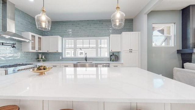 kitchen featuring tasteful backsplash, wall chimney exhaust hood, light countertops, white cabinetry, and a sink