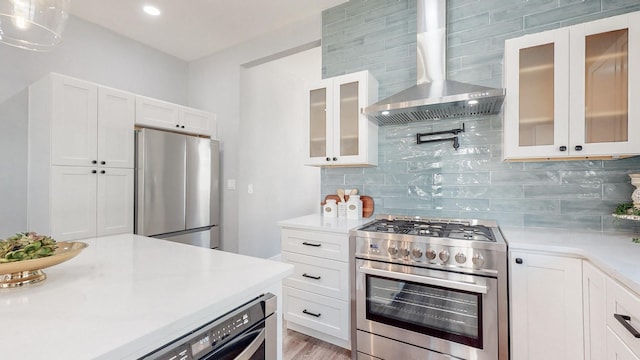 kitchen featuring light countertops, decorative backsplash, appliances with stainless steel finishes, white cabinets, and wall chimney range hood