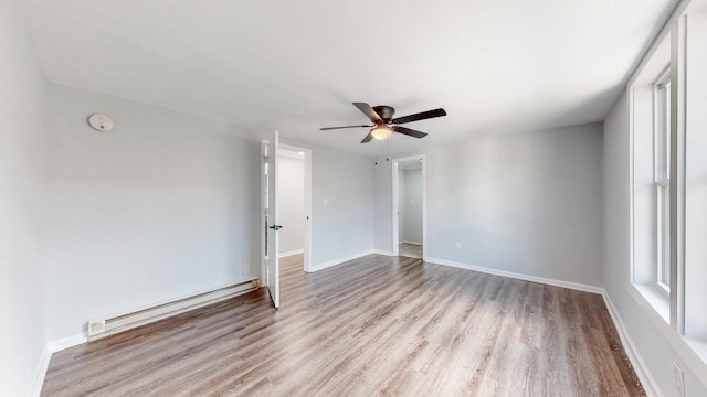 spare room with ceiling fan, baseboard heating, wood finished floors, and baseboards