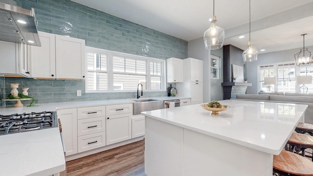 kitchen with a breakfast bar area, a sink, light countertops, wall chimney range hood, and backsplash