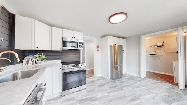 kitchen featuring appliances with stainless steel finishes, white cabinetry, a sink, and light stone countertops