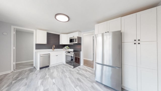 kitchen with a sink, white cabinetry, baseboards, light countertops, and appliances with stainless steel finishes