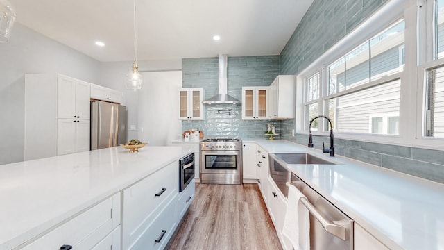 kitchen featuring tasteful backsplash, white cabinets, wall chimney exhaust hood, appliances with stainless steel finishes, and light countertops